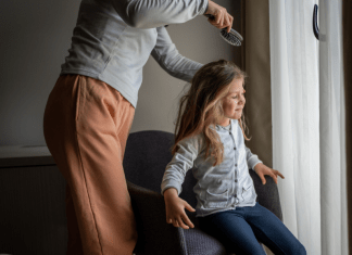 Parent hesitates to brush daughter's hair who is squirming in her seat.