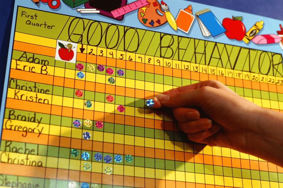 Child puts a sticker on a good behavior chart in first grade.