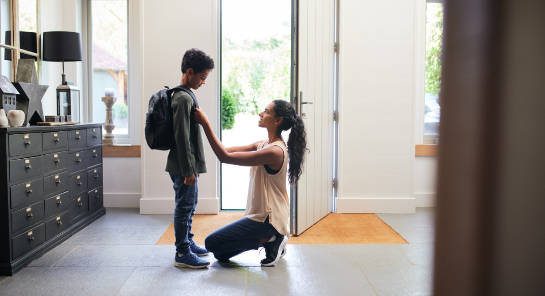 A mom kneels down to help her son with his backpack before school in the morning.