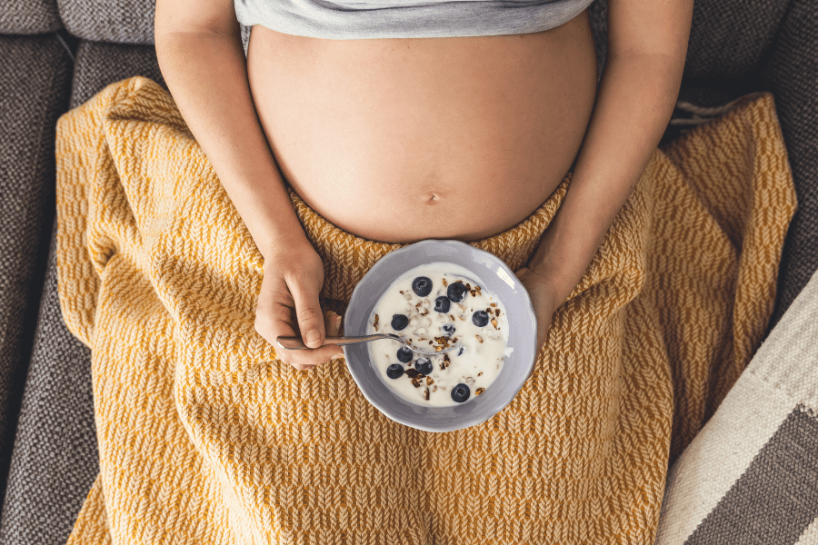 Pregnant woman holds bowl of yogurt, granola, and berries next to her belly.