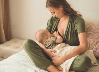 Mother wears nursing-friendly romper while breastfeeding her baby.