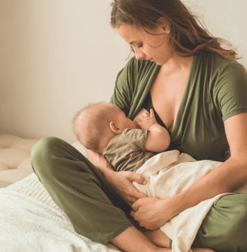 Mother wears nursing-friendly romper while breastfeeding her baby.