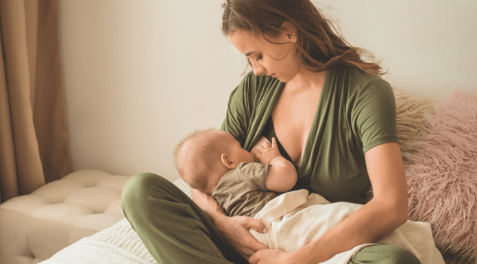 Mother wears nursing-friendly romper while breastfeeding her baby.