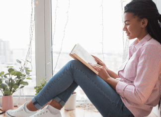 A mom reads a book by the window.