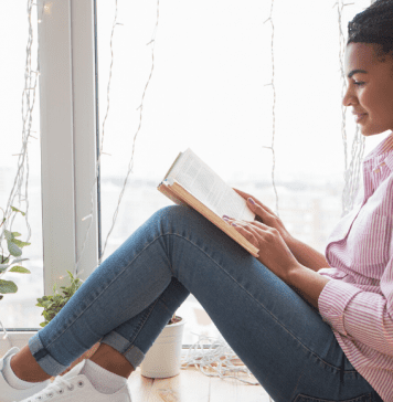 A mom reads a book by the window.