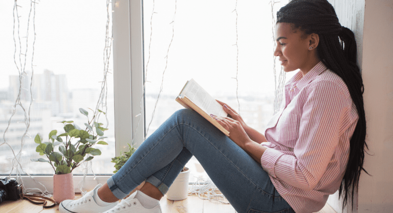 A mom reads a book by the window.