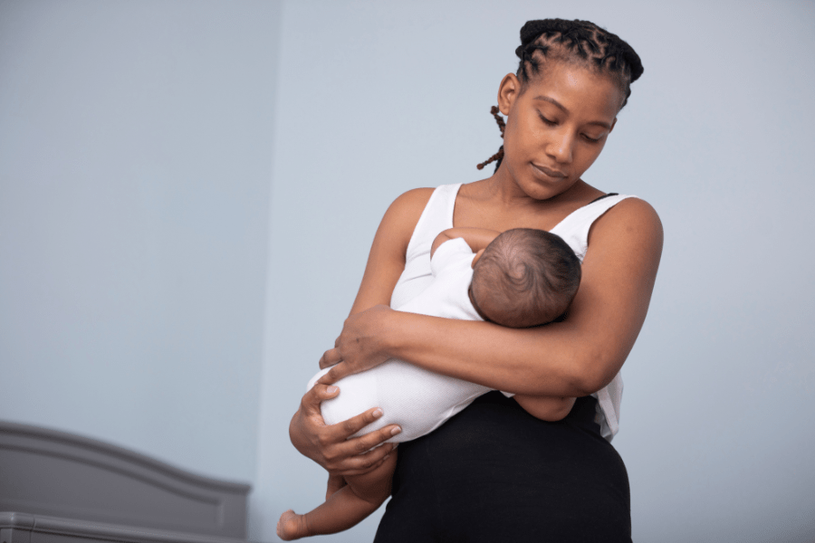 Mother holds her baby in her arms, and looks down at her baby while struggling to breastfeed.