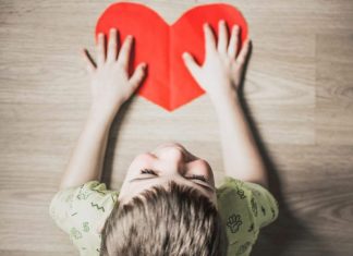 A boy has his hands on top of a paper heart cut-out.