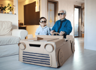 Grandpa and grandson sit in a homemade cardboard vehicle with sunglasses on.