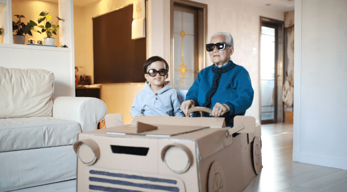 Grandpa and grandson sit in a homemade cardboard vehicle with sunglasses on.