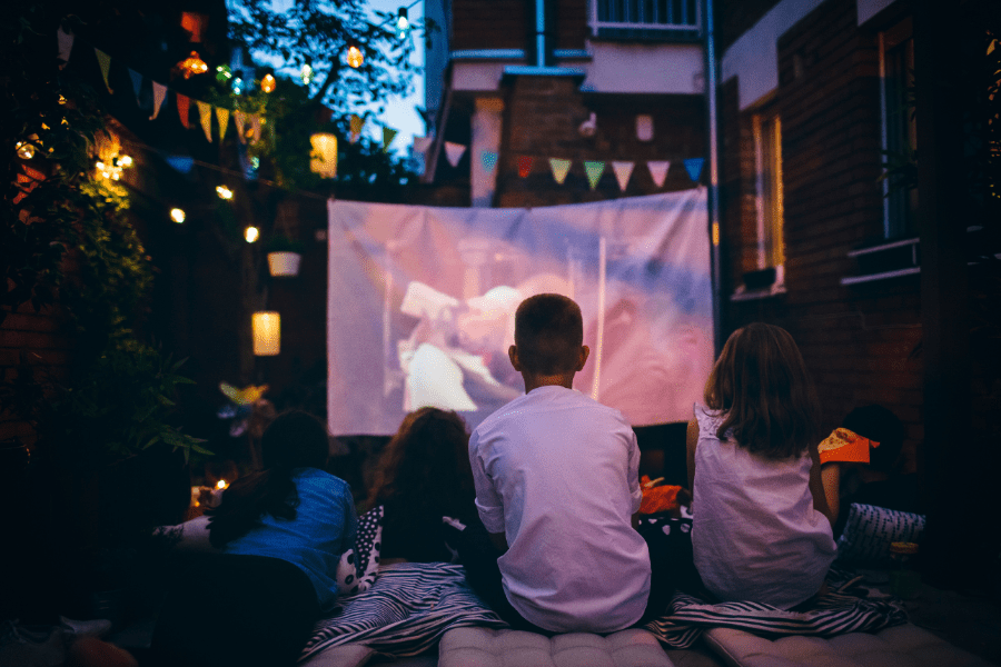 Dad and kids sit on blankets and pillows while watching a drive-in movie.