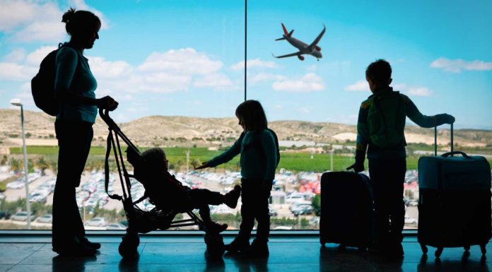 The silhouette of a mom with her toddler child and two older kids at an airport, standing with luggage.