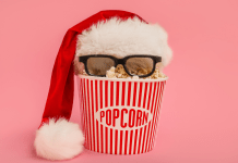 A popcorn bucket with a Santa hat and 3D glasses on a pink background.