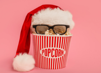 A popcorn bucket with a Santa hat and 3D glasses on a pink background.