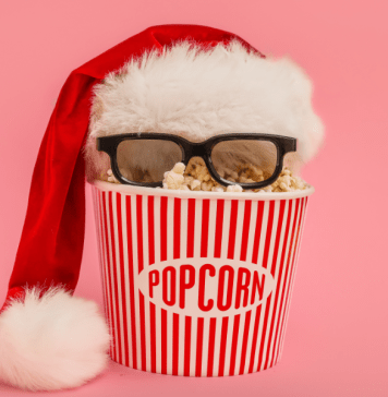 A popcorn bucket with a Santa hat and 3D glasses on a pink background.