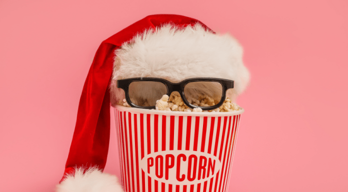 A popcorn bucket with a Santa hat and 3D glasses on a pink background.