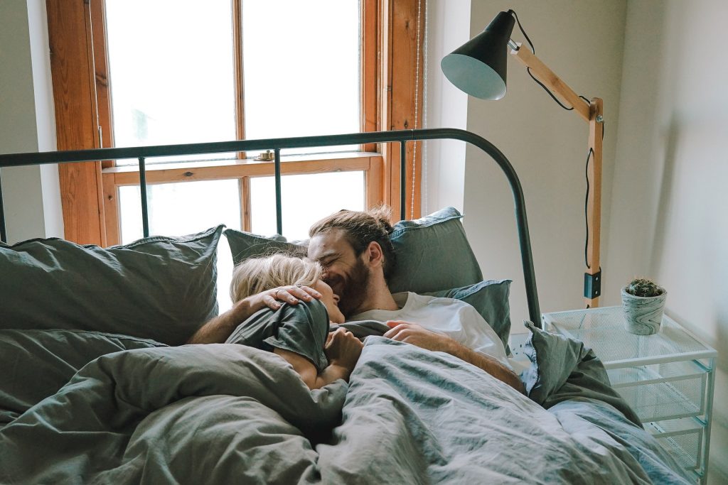 A couple cuddle and laugh in bed together.