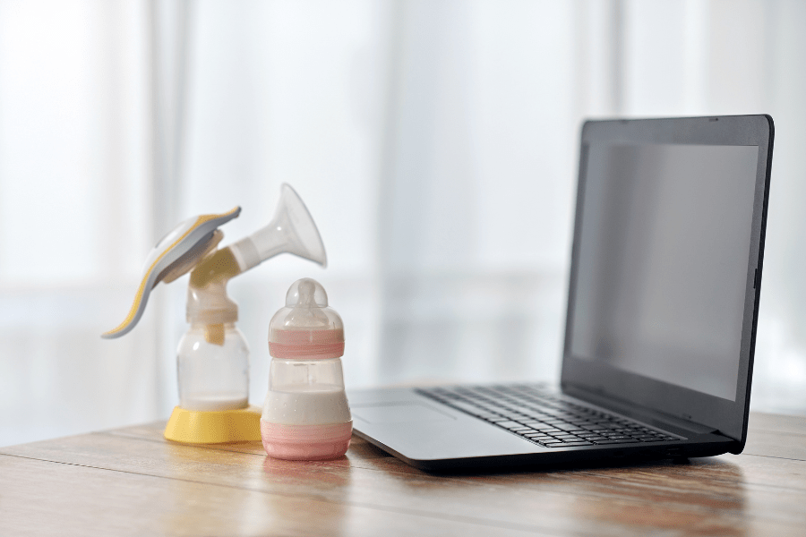 Breast pump bottle, baby milk bottle, and a laptop sit on a desk.