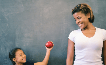 Child gives an apple to her teacher for a back-to-school teacher gift.