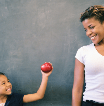 Child gives an apple to her teacher for a back-to-school teacher gift.