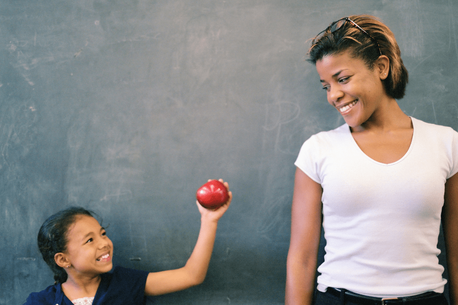 Child gives an apple to her teacher for a back-to-school teacher gift.