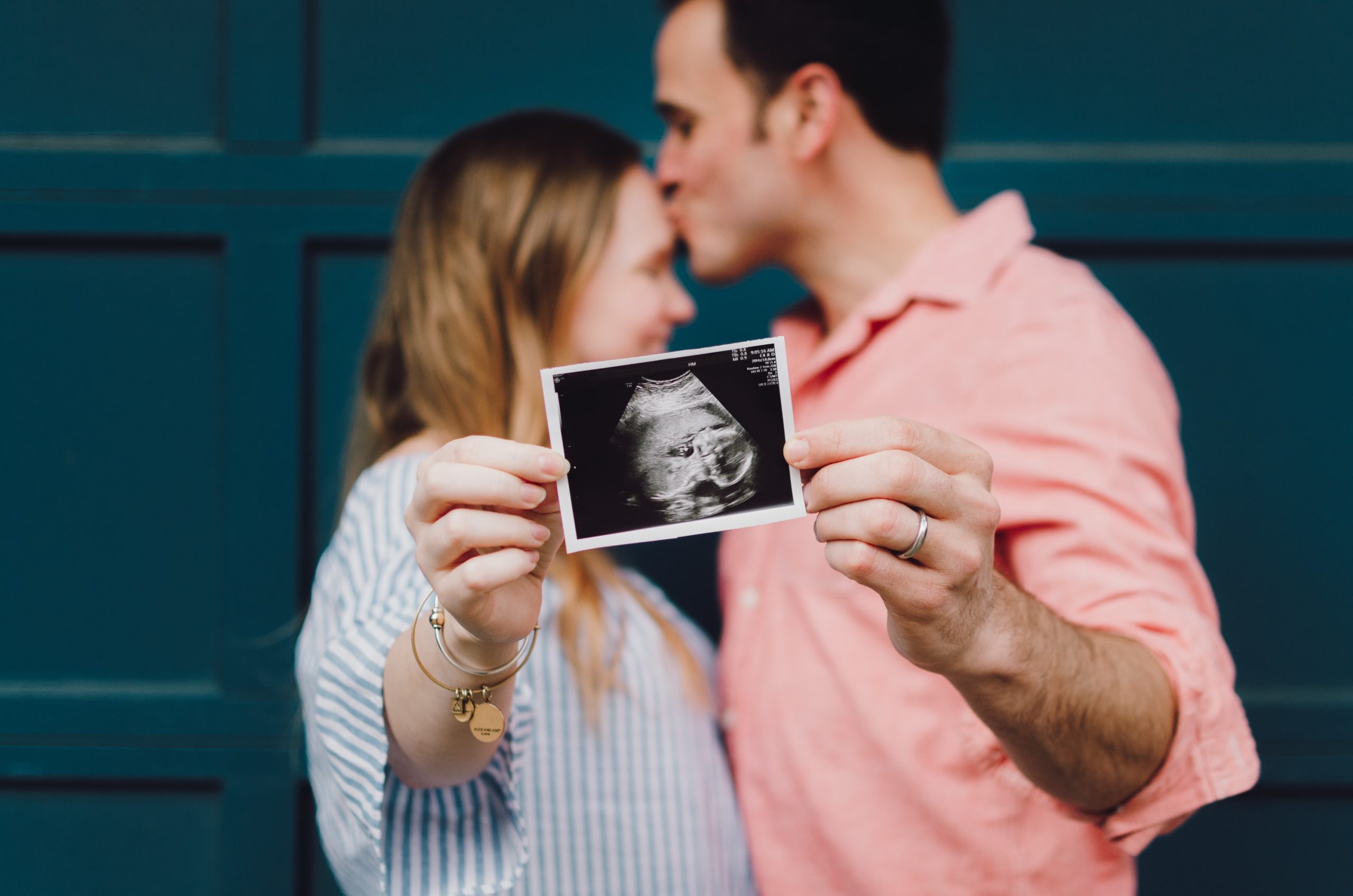 A couple kisses and holds a sonogram.