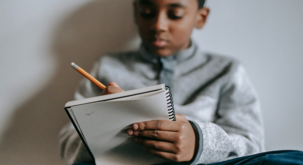 A boy writes a letter in a notebook.