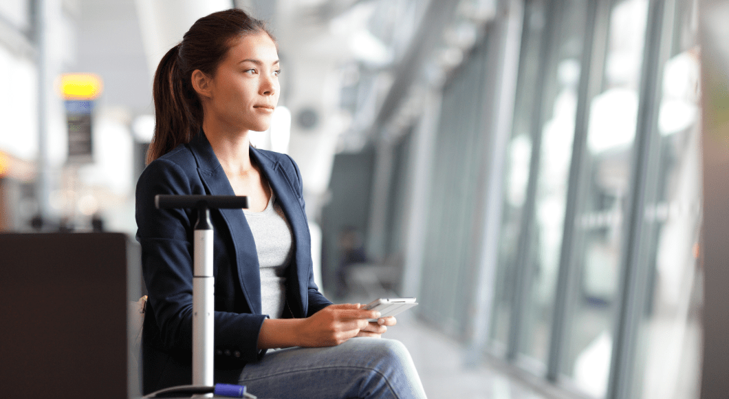 A woman sits at the airport with her luggage and phone.