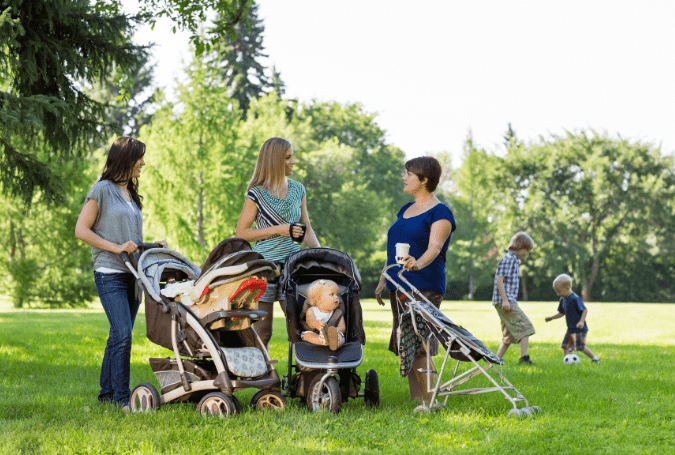 moms with kids in strollers at park talking