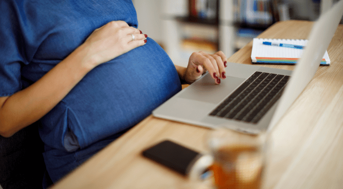 A pregnant woman sits at a counter with a computer.