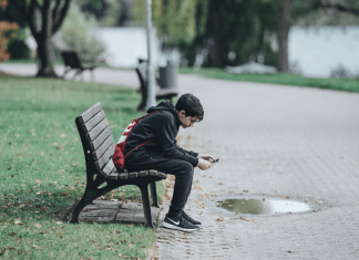 A teenage boy sits on a bench looking at his phone.