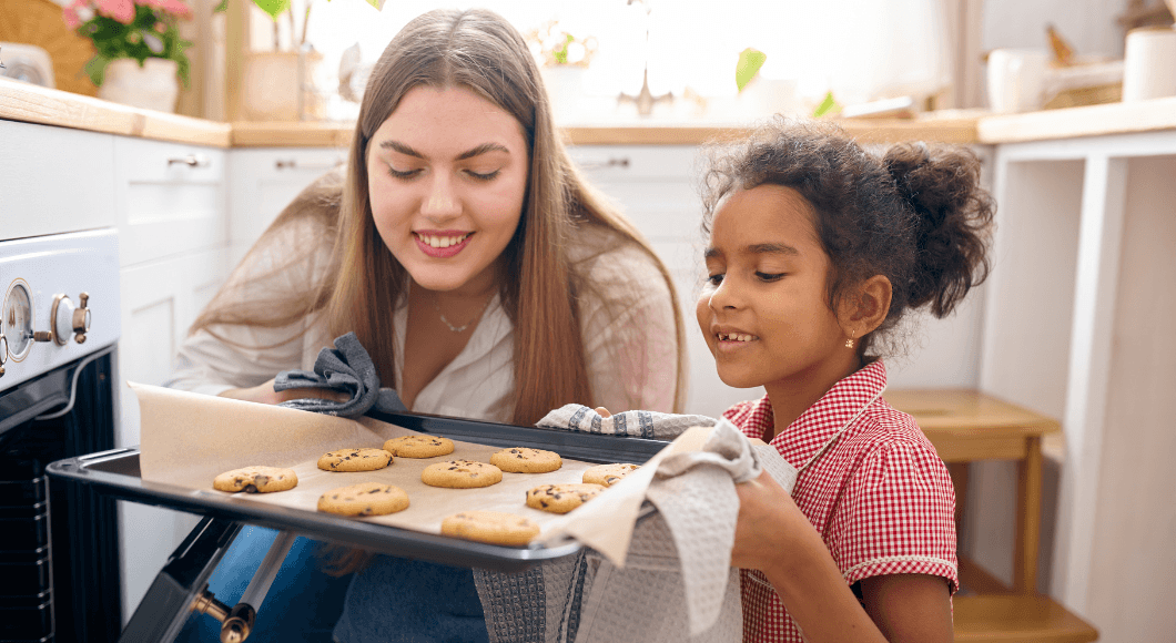 A mom and daughter pull cookies out of the oven.