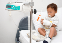 A little boy with neutropenia sits on a hospital bed hooked up to a monitor.