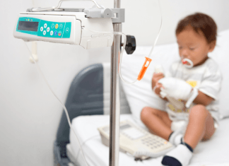 A little boy with neutropenia sits on a hospital bed hooked up to a monitor.