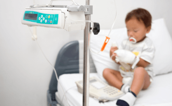 A little boy with neutropenia sits on a hospital bed hooked up to a monitor.