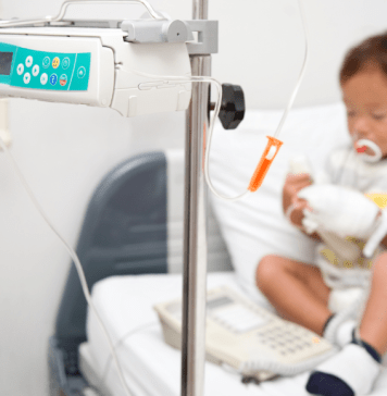 A little boy with neutropenia sits on a hospital bed hooked up to a monitor.