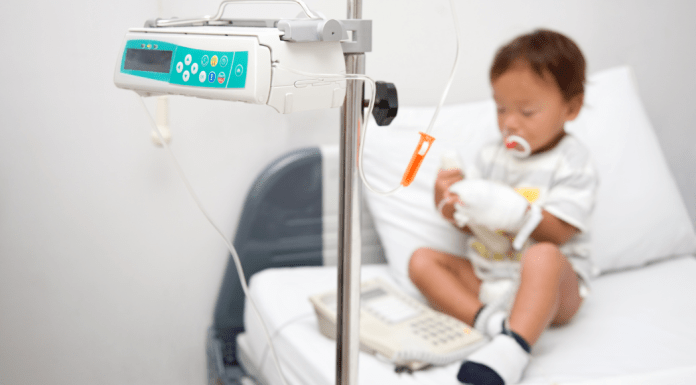 A little boy with neutropenia sits on a hospital bed hooked up to a monitor.