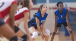 Young women play volleyball on a court.