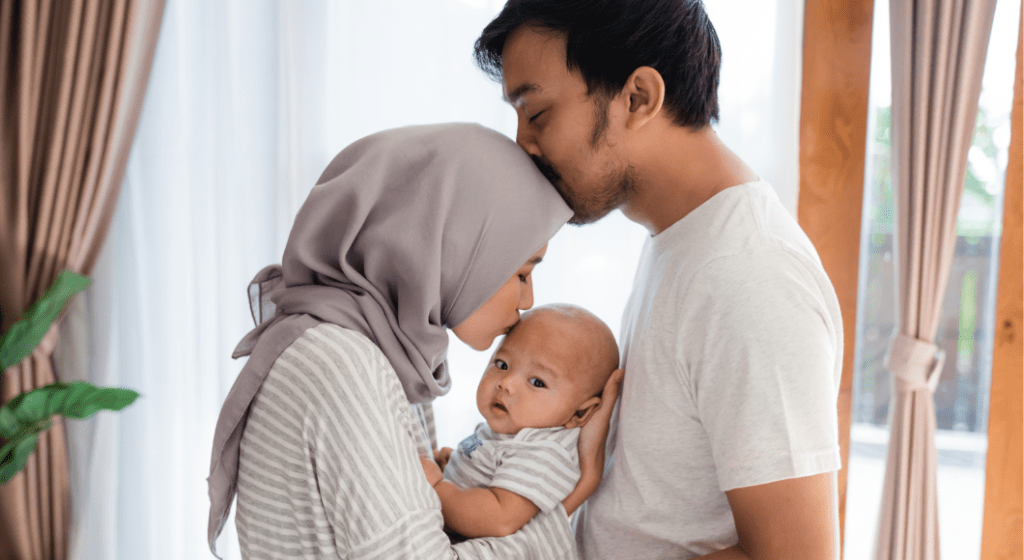 A father and mother tenderly embrace each other and their baby.