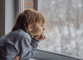 A young boy looks out the window to winter weather.