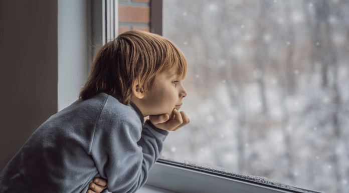 A young boy looks out the window to winter weather.