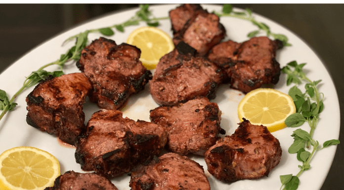 Grilled lamb chops resting on a white plate with lemons and green garnish