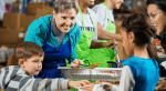 A mother and young son serve food to a mother and daughter.