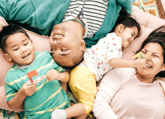 A happy family laughs together on the floor.