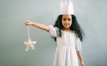 Little girl holds a wand and wears a princess crown and gown.