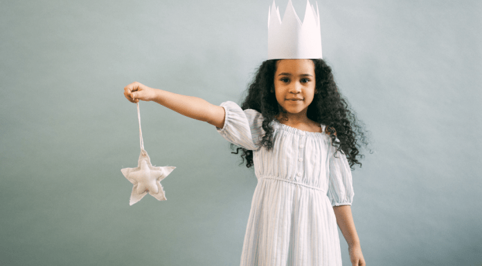 Little girl holds a wand and wears a princess crown and gown.