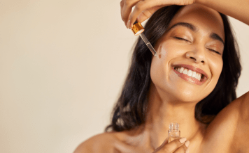 A woman applies serum to her face.