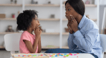 A speech pathologist models vowel sounds to a little girl who mimics her mouth shape.