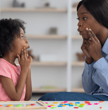 A speech pathologist models vowel sounds to a little girl who mimics her mouth shape.