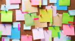 A bulletin board covered in colorful sticky notes, washi tape, and thumbtacks.